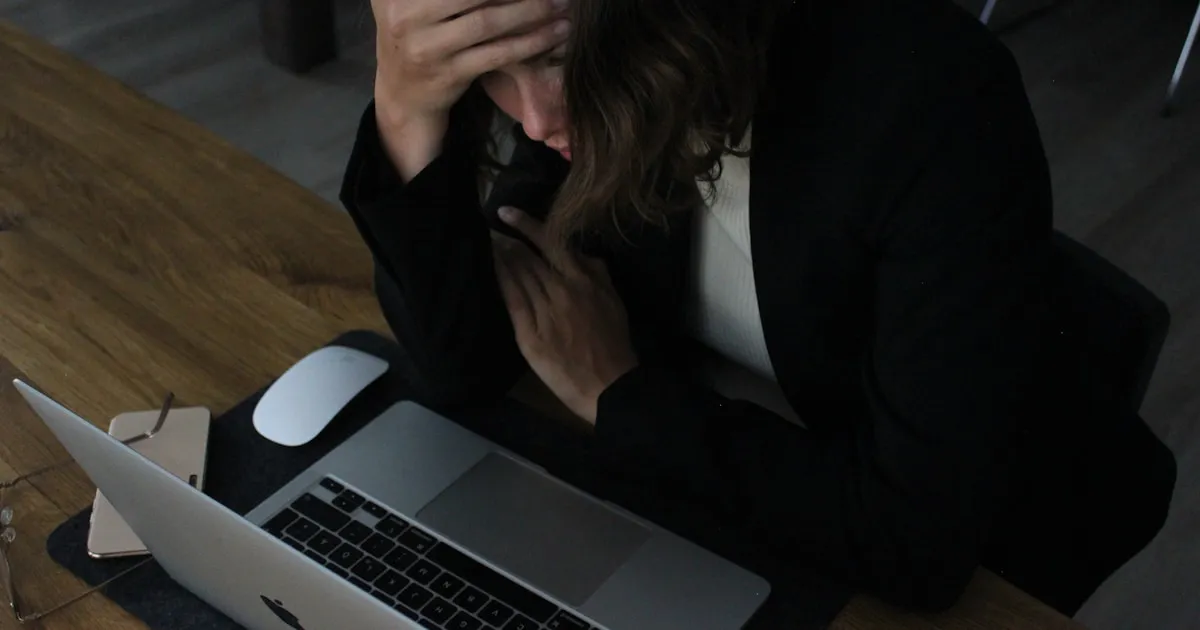 An exhausted woman with head in hands sitting at a desk, conveying the emotional weight of caregiver burnout