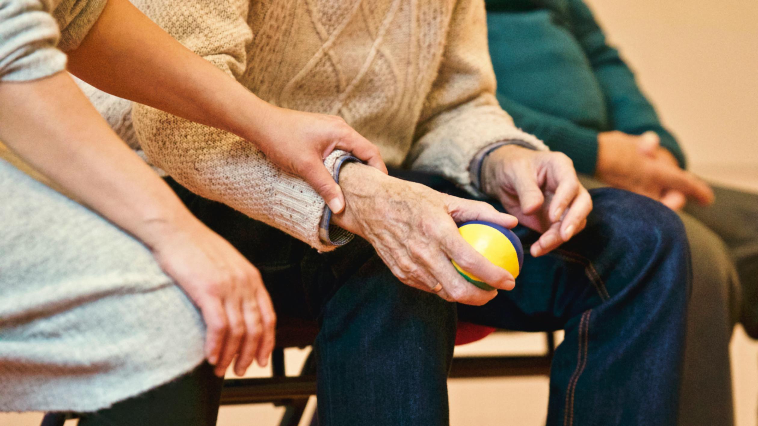 A caregiver's hand gently resting on an elderly person's arm during a supportive conversation